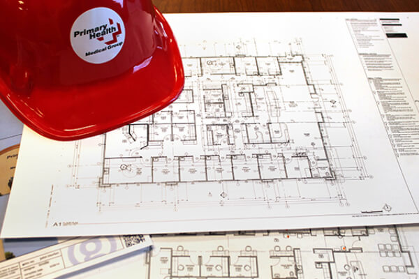 Primary Health construction hat on top of blueprints for the new Orchard Urgent Care Clinic