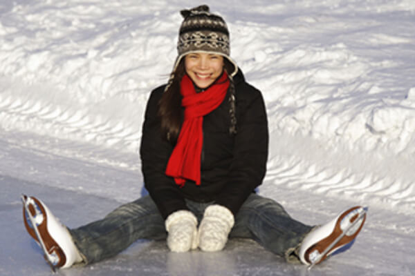 young woman sitting on ice, dressed in winter clothes wearing ice skates